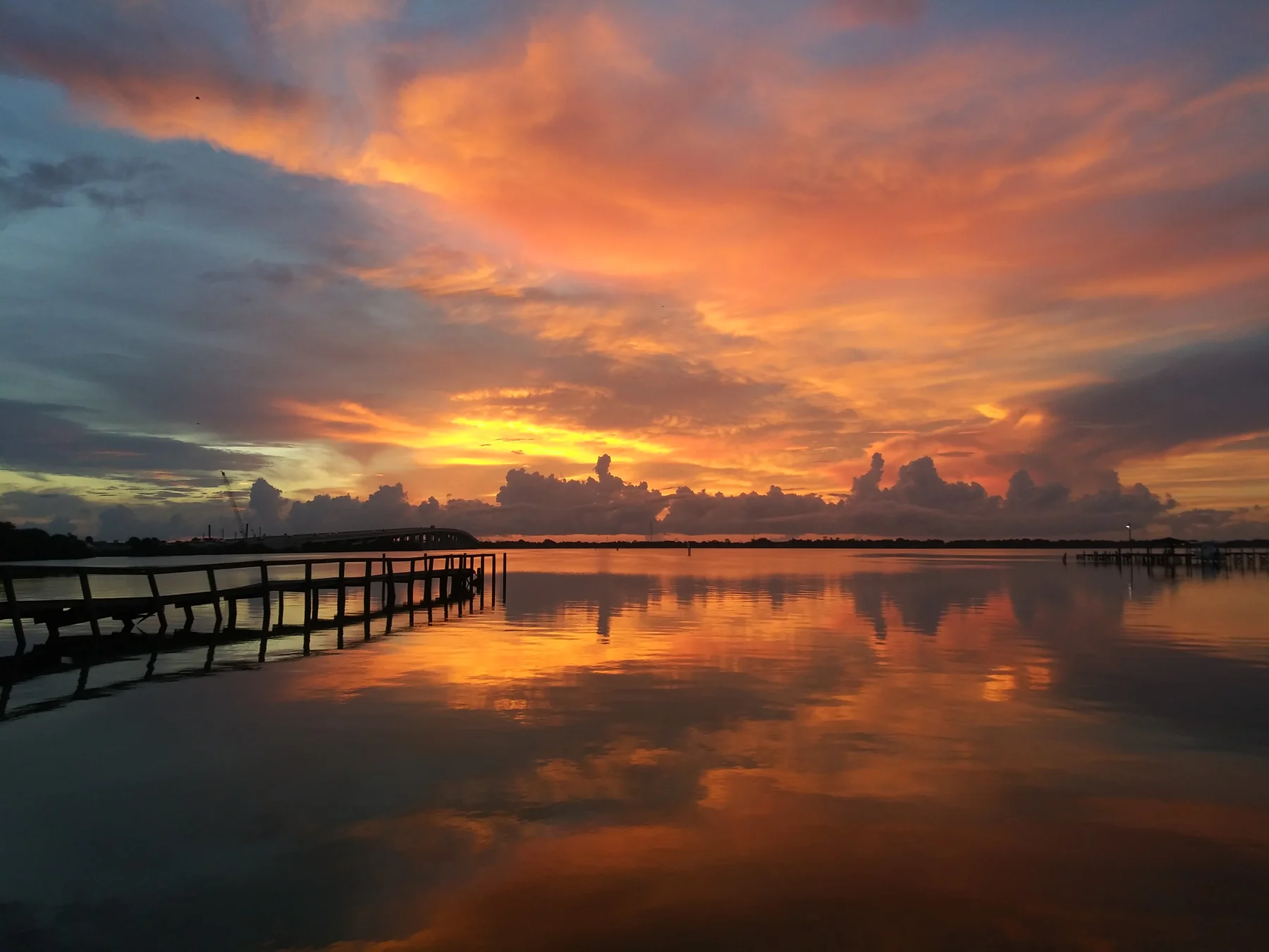 Orange morning sky reflected in the water beside a Space Coast pier